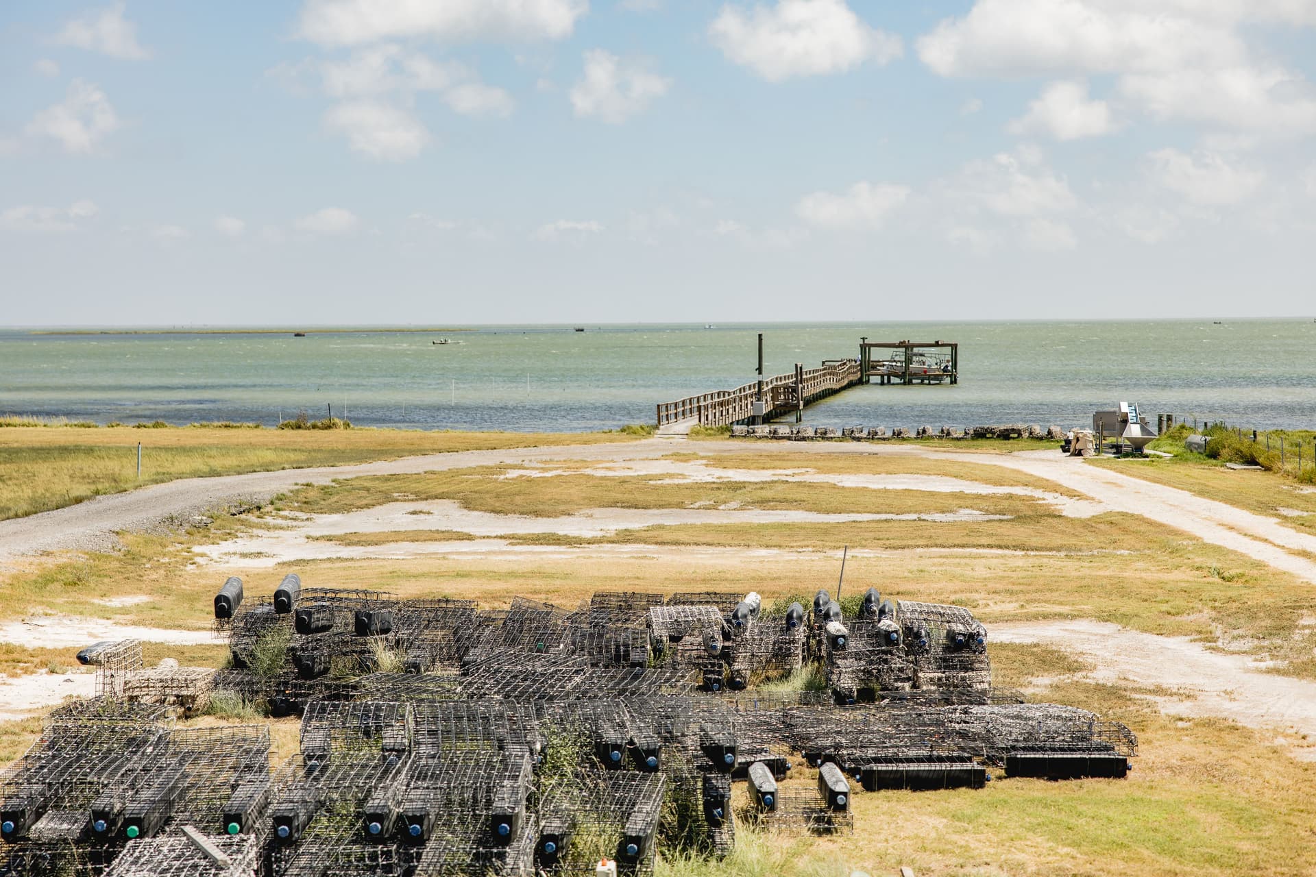 Rows of oyster farming cages on the shoreline of a Texas oyster ranch, with a pier extending into a calm coastal bay
