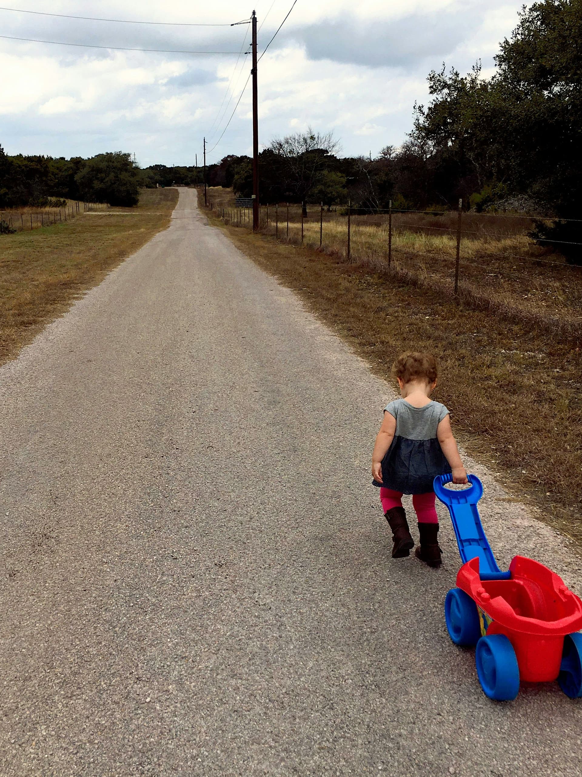 Young child pulling a toy wagon down a quiet country road through rural Texas ranch land